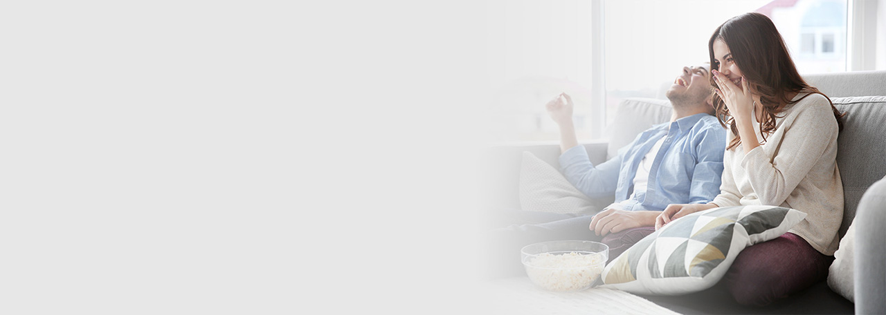 Besijuokianti pora, kuri sėdi ant sofos su spragintais kukurūzais.