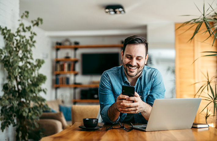 Vyras, žiūrintis namie į savo mobilųjį telefoną
